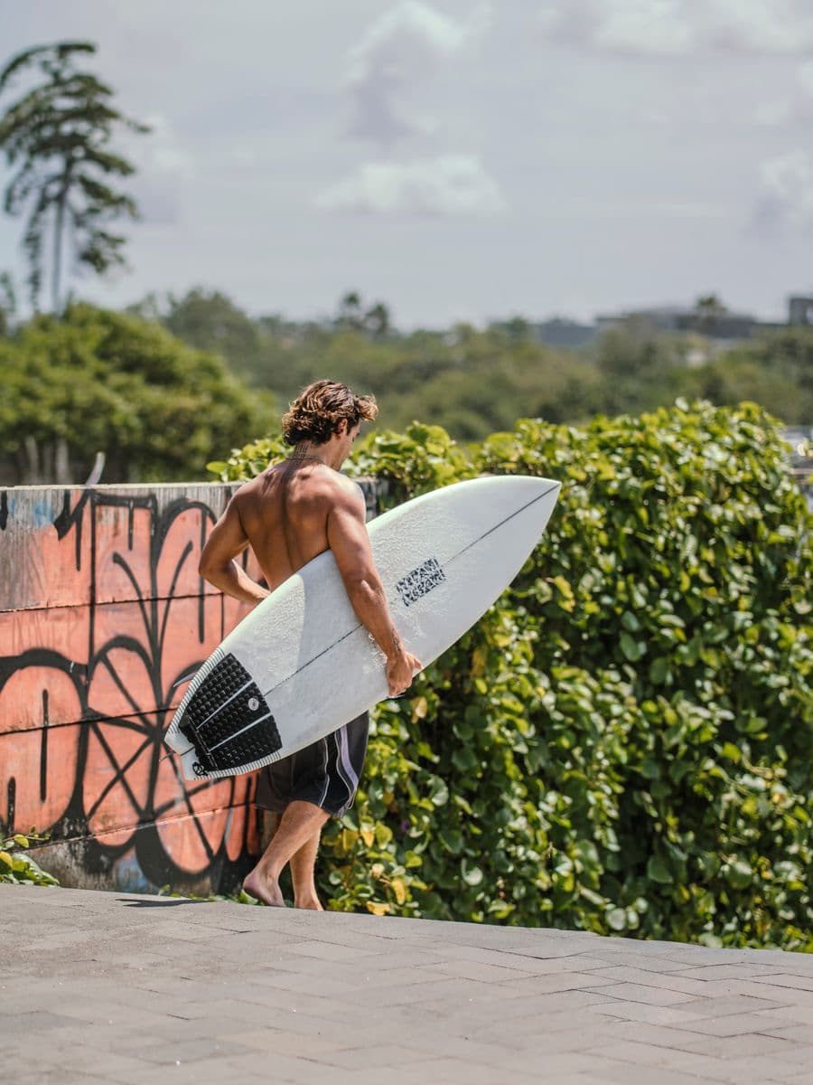 Surfer carrying his board along Pererenan's graffiti-lined beach lane